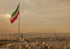 Iranian flag waving over a city skyline with mountains in the background