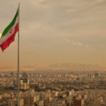 Iranian flag waving over a city skyline with mountains in the background