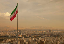 Trump’s Bold Move: Iran’s Military Backbone Crushed Iranian flag waving over a city skyline with mountains in the background