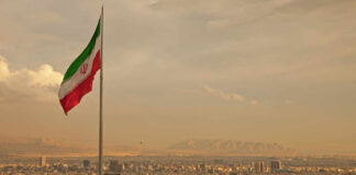 Iranian flag waving over a city skyline with mountains in the background