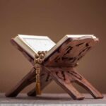 A beautifully crafted wooden stand holding an open Quran with prayer beads
