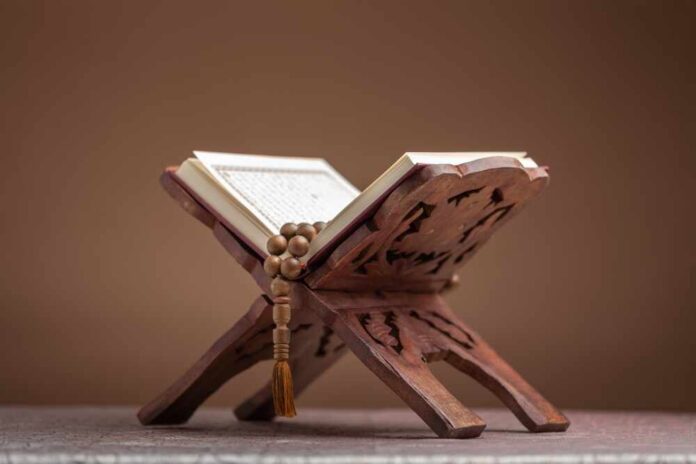 shutterstock_2288142353.jpg A beautifully crafted wooden stand holding an open Quran with prayer beads