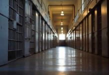 Empty prison corridor with metal cell doors visible