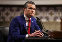 Man in suit sitting at a desk with microphone