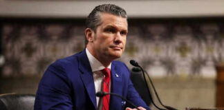 Man in suit sitting at a desk with microphone