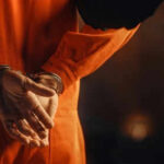 Person in orange jumpsuit with hands cuffed behind