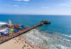 Aerial view of a busy beach pier with amusement rides and people enjoying the ocean