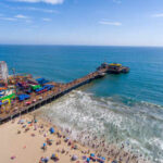 Aerial view of a busy beach pier with amusement rides and people enjoying the ocean