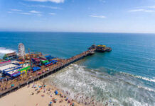 Aerial view of a busy beach pier with amusement rides and people enjoying the ocean