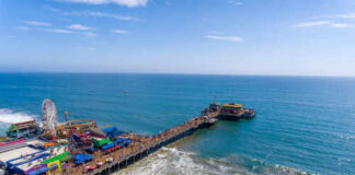 Aerial view of a busy beach pier with amusement rides and people enjoying the ocean
