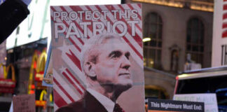 Crowd holding a sign that reads 'Protect This Patriot' with an image of a man