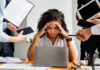 A stressed woman at a desk surrounded by multiple devices and people