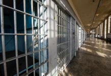 Interior view of a prison corridor with jail cells and sunlight streaming through windows