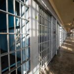 Interior view of a prison corridor with jail cells and sunlight streaming through windows