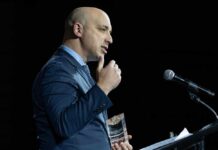 A man in a blue suit speaking at a podium while holding an award