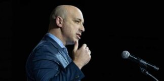 A man in a blue suit speaking at a podium while holding an award