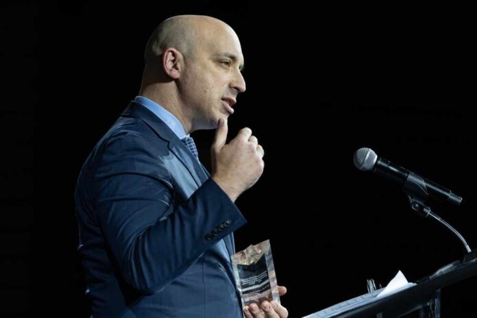 A man in a blue suit speaking at a podium while holding an award