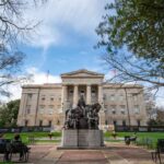 Historic building with a statue in front and people sitting on benches
