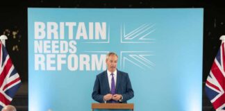 A politician delivering a speech at a podium with British flags in the background