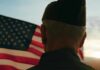 A veteran in uniform standing in front of an American flag at sunset