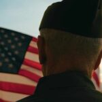 A veteran in uniform standing in front of an American flag at sunset
