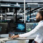 A man working at a computer workstation with multiple screens displaying data visualizations
