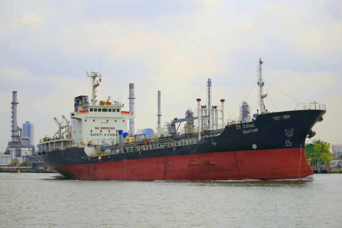 A cargo ship navigating through a port with industrial buildings in the background