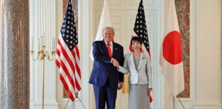 Two political leaders shaking hands in front of flags