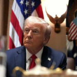 Man in suit sitting with flag background and eagle decoration