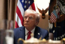 Man in suit sitting with flag background and eagle decoration
