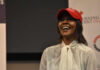 A woman wearing a red cap smiling and speaking at an event