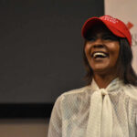 A woman wearing a red cap smiling and speaking at an event