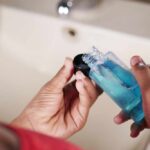 Person holding a bottle of blue liquid in a bathroom