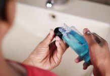 Person holding a bottle of blue liquid in a bathroom