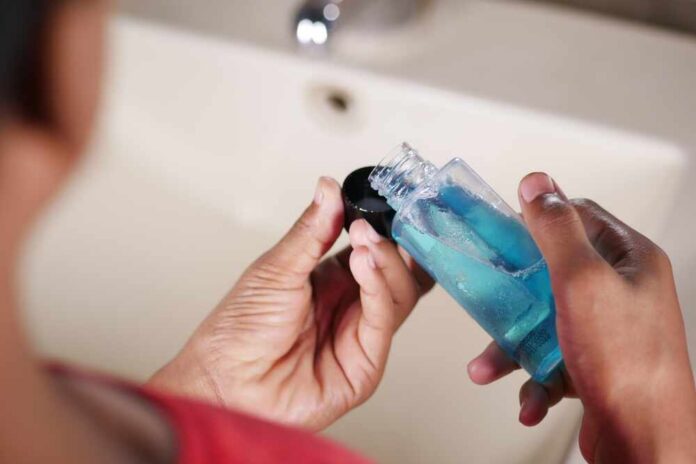 Person holding a bottle of blue liquid in a bathroom