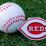 A baseball and a Cincinnati Reds logo on green grass