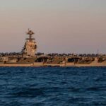 An aircraft carrier with the number 78 anchored in the ocean during sunset