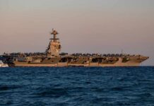 An aircraft carrier with the number 78 anchored in the ocean during sunset