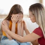 A mother comforting her distressed daughter who is covering her face