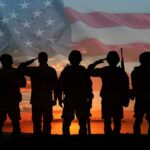 Silhouetted soldiers saluting against an American flag backdrop at sunset