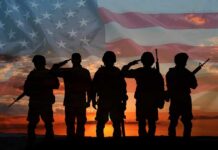 Silhouetted soldiers saluting against an American flag backdrop at sunset