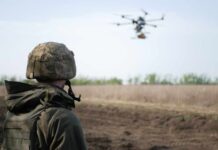 A soldier observing a drone flying over a field