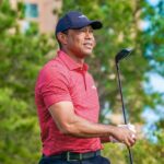 A golfer holding a club outdoors, wearing a red striped shirt