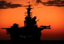 Silhouette of a naval aircraft carrier against a vibrant sunset