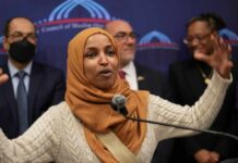 A woman in a hijab passionately speaking at a podium with a diverse group in the background