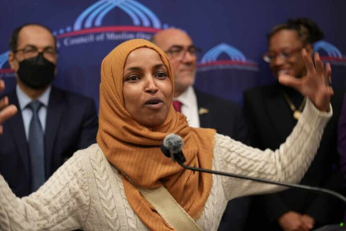 A woman in a hijab passionately speaking at a podium with a diverse group in the background