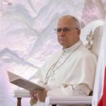 Pope seated in a ceremonial chair with flags in the background
