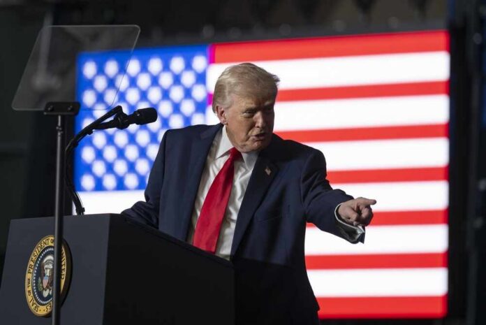 shutterstock_2734662775.jpg A man in a suit gestures while speaking at a podium with an American flag in the background