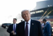 A political figure standing outdoors with a serious expression