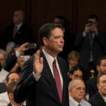 A man raising his right hand in a congressional hearing setting